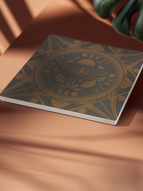Square ceramic coaster featuring a detailed copper dragonfly design centered in a medallion, surrounded by moon phases and Art Nouveau patterns on a charcoal black background, with cork backing.